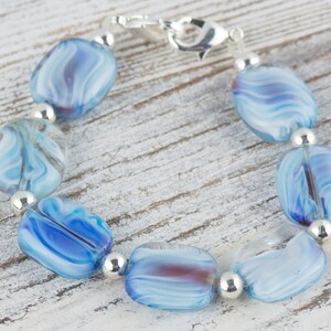 May include: A bracelet made of blue and white swirled glass beads with silver spacers and a silver clasp.
