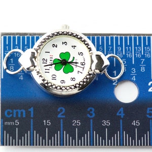 Peut inclure: Une montre argent&eacute;e avec un cadran blanc et un tr&egrave;fle vert. La montre mesure 2,5 cm de diam&egrave;tre et a un fermoir en forme de c&oelig;ur.