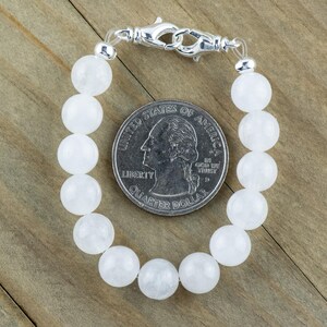 May include: A white gemstone bracelet with a silver clasp. The bracelet is made of round beads and is about the size of a quarter.