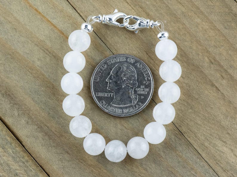 May include: A white gemstone bracelet with a silver clasp. The bracelet is made of round beads and is about the size of a quarter.