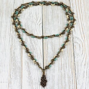 May include: A double-strand necklace with a pendant. The necklace is made of small, light blue and white beads, and the pendant is a bronze-coloured, intricate design.