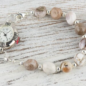 May include: A silver watch with a white face and black numbers is attached to a bracelet made of brown and white stones.