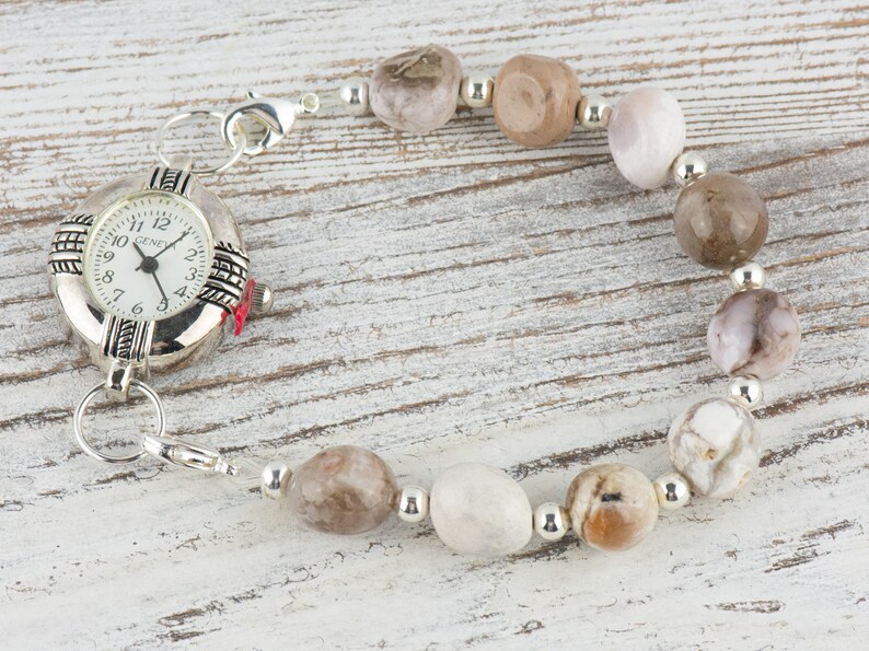 May include: A silver watch with a white face and black numbers is attached to a bracelet made of brown and white stones.