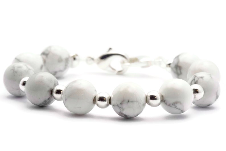May include: A bracelet featuring white and grey marbled stone beads, interspersed with silver-coloured metal beads and a silver clasp. The beads are round. A piece of jewellery.