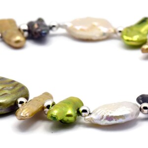 K&ouml;nnte beinhalten: Ein Armband aus gr&uuml;nen, braunen und wei&szlig;en S&uuml;&szlig;wasserperlen mit silbernen Akzenten. Das Armband verf&uuml;gt &uuml;ber eine Vielzahl von Formen und Gr&ouml;&szlig;en von Perlen, darunter runde, ovale und quadratische.