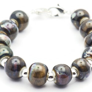 May include: A bracelet made of brown and black ceramic beads with silver accents. The beads have a mottled, iridescent finish.