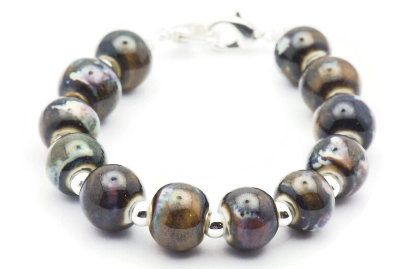 May include: A bracelet made of brown and black ceramic beads with silver accents. The beads have a mottled, iridescent finish.