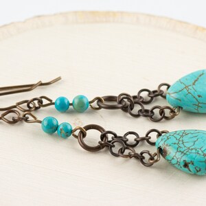 May include: Turquoise and bronze earrings with a chain and beads. The earrings have a teardrop shape and are made with natural turquoise stones.