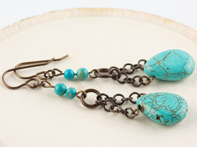 May include: Turquoise and bronze earrings with a chain and beads. The earrings have a teardrop shape and are made with natural turquoise stones.