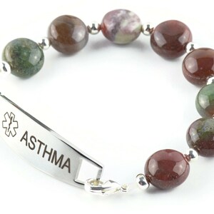 May include: A silver medical alert bracelet with a red and green agate bead bracelet. The bracelet has a silver tag that reads "ASTHMA" with a medical symbol.