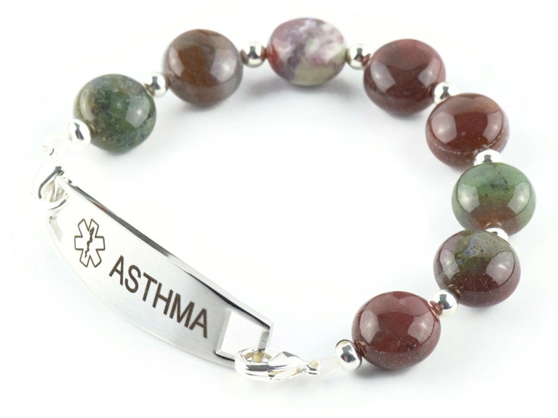 May include: A silver medical alert bracelet with a red and green agate bead bracelet. The bracelet has a silver tag that reads "ASTHMA" with a medical symbol.