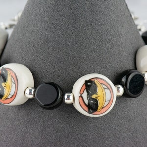May include: A white and black bracelet with cartoon duck faces on the white beads. The bracelet is made of ceramic beads and silver spacers.