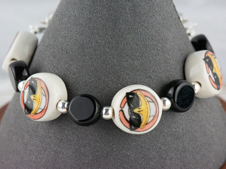 May include: A white and black bracelet with cartoon duck faces on the white beads. The bracelet is made of ceramic beads and silver spacers.