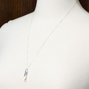Pu&ograve; includere: Una collana a catena d'argento con un ciondolo di cristallo trasparente. Il ciondolo ha la forma di un prisma rettangolare.