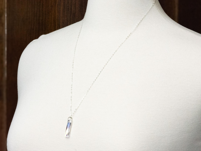 Pu&ograve; includere: Una collana a catena d'argento con un ciondolo di cristallo trasparente. Il ciondolo ha la forma di un prisma rettangolare.
