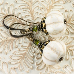 May include: White and gold tone earrings with green glass beads. The earrings feature a round, white bead with a textured surface.