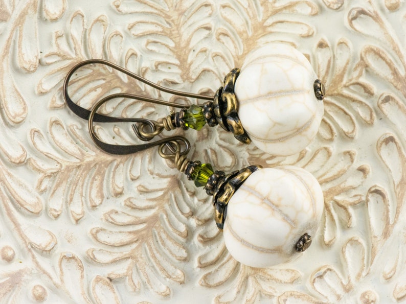 May include: White and gold tone earrings with green glass beads. The earrings feature a round, white bead with a textured surface.