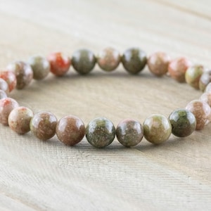 May include: A bracelet made of round, multi-colored, speckled beads. The beads are a mix of green, brown, and pink.
