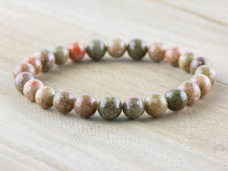 May include: A bracelet made of round, multi-colored, speckled beads. The beads are a mix of green, brown, and pink.