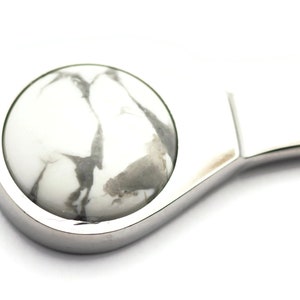 May include: A silver bottle opener with a white and grey marble-like stone inset.
