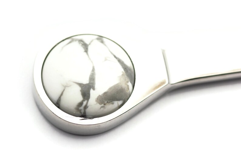 May include: A silver bottle opener with a white and grey marble-like stone inset.