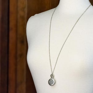 May include: A silver necklace with a round pendant featuring a detailed design. The pendant is attached to a silver chain.