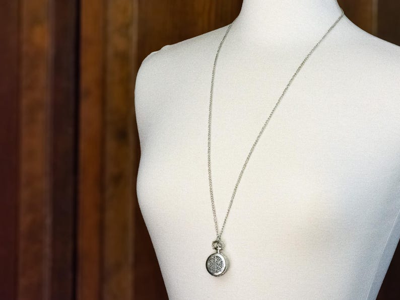 May include: A silver necklace with a round pendant featuring a detailed design. The pendant is attached to a silver chain.