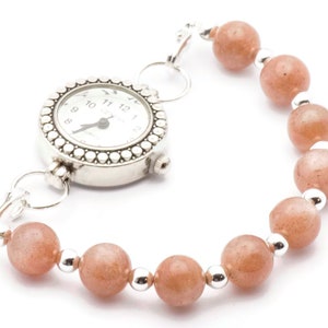 May include: A silver watch with a white face and black numbers is attached to a bracelet made of orange beads and silver spacers.
