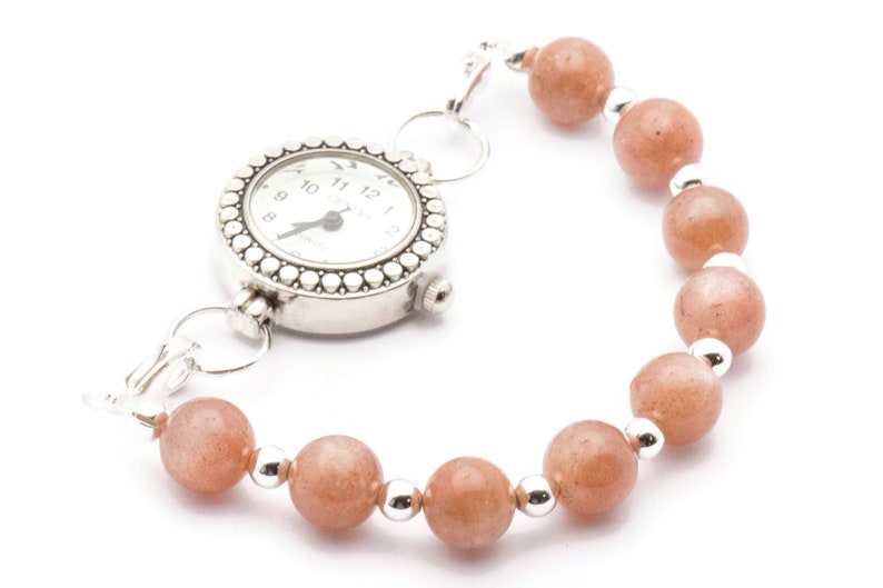 May include: A silver watch with a white face and black numbers is attached to a bracelet made of orange beads and silver spacers.