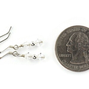 May include: A pair of silver earrings with clear crystal beads and silver hooks. The earrings are shown next to a US quarter for size comparison.