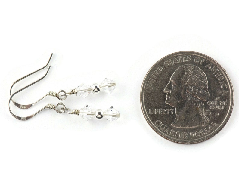 May include: A pair of silver earrings with clear crystal beads and silver hooks. The earrings are shown next to a US quarter for size comparison.