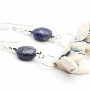 May include: A pair of silver earrings with blue lapis lazuli stones and white ceramic flower charms.