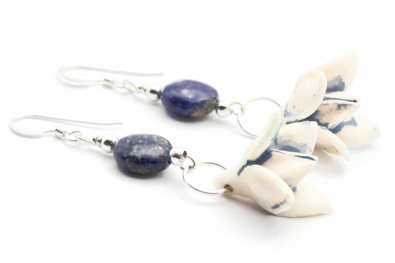 May include: A pair of silver earrings with blue lapis lazuli stones and white ceramic flower charms.