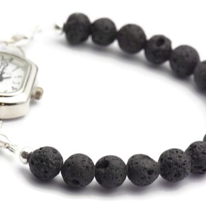 May include: A silver watch with a square face and black lava rock beads attached to the band.