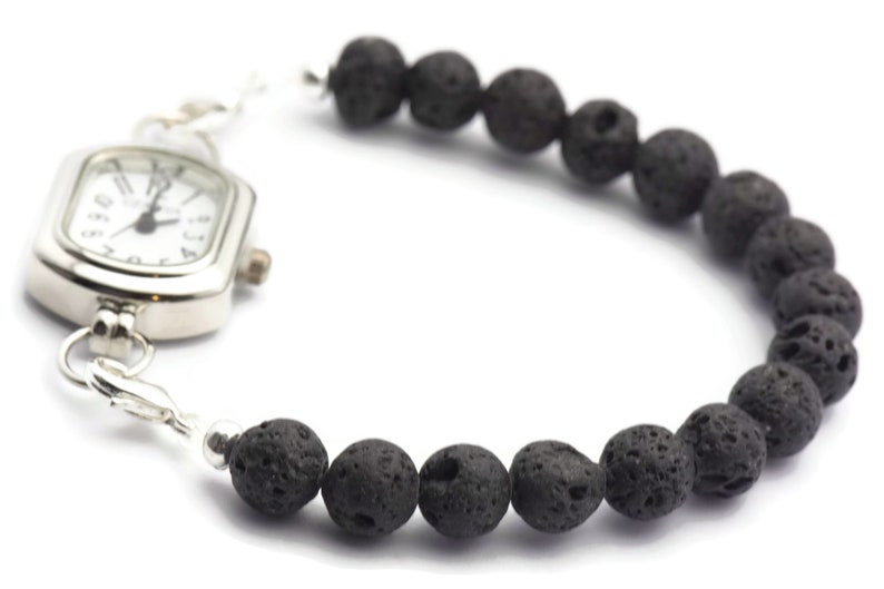 May include: A silver watch with a square face and black lava rock beads attached to the band.
