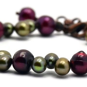 May include: A bracelet made of dark green, burgundy, and iridescent pearls. The pearls are strung on a brown cord and secured with a clasp.