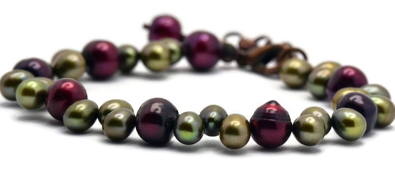 May include: A bracelet made of dark green, burgundy, and iridescent pearls. The pearls are strung on a brown cord and secured with a clasp.