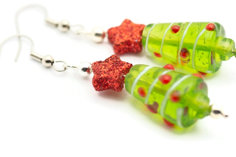 Op de afbeelding: Een paar groene glazen kerstboom oorbellen met rode glittersterren. De oorbellen zijn op een witte achtergrond.
