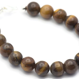 Op de afbeelding: Een bruine en gouden tijgeroog kralen armband met een zilveren sluiting.