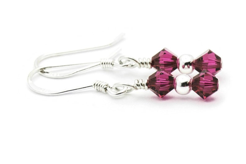 Puede incluir: Un par de pendientes de plata con dos peque&ntilde;as cuentas de cristal rosa oscuro en cada pendiente.