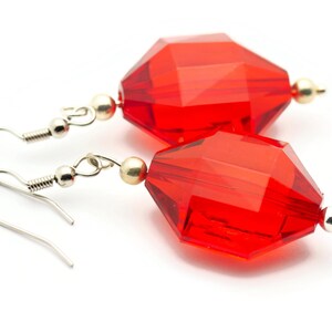 May include: A pair of red crystal earrings with silver hooks. The crystals are faceted and have a geometric shape.