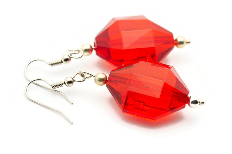 May include: A pair of red crystal earrings with silver hooks. The crystals are faceted and have a geometric shape.