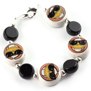 May include: A bracelet with black and white ceramic beads. The white beads feature a cartoon duck wearing sunglasses.