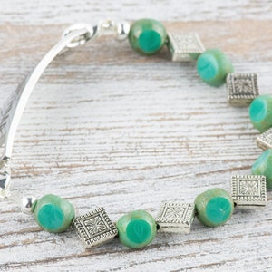 Pu&ograve; includere: Un braccialetto d'argento con una chiusura d'argento e perline di vetro verde. Le perline sono separate da un ciondolo quadrato d'argento.