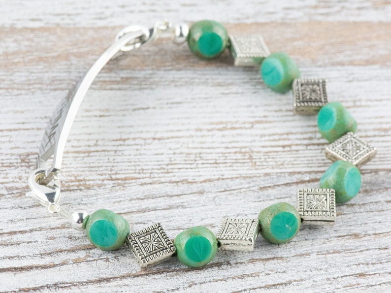Pu&ograve; includere: Un braccialetto d'argento con una chiusura d'argento e perline di vetro verde. Le perline sono separate da un ciondolo quadrato d'argento.