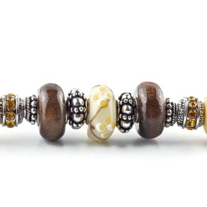 May include: A brown and cream charm bracelet with silver beads and spacers. The bracelet features a variety of charms, including wooden beads, glass beads, and metal beads.