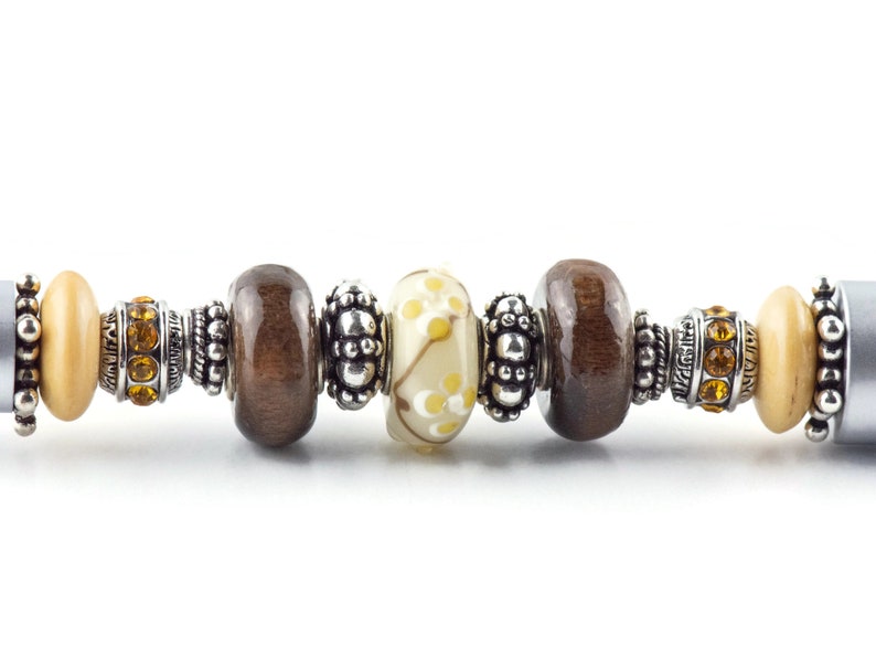 May include: A brown and cream charm bracelet with silver beads and spacers. The bracelet features a variety of charms, including wooden beads, glass beads, and metal beads.