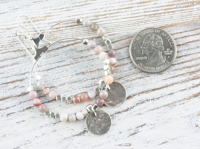 Pu&ograve; includere: Un paio di orecchini a cerchio d'argento con perline di agata rosa e bianca e ciondoli d'argento. Gli orecchini sono circa delle dimensioni di una moneta da 25 centesimi.