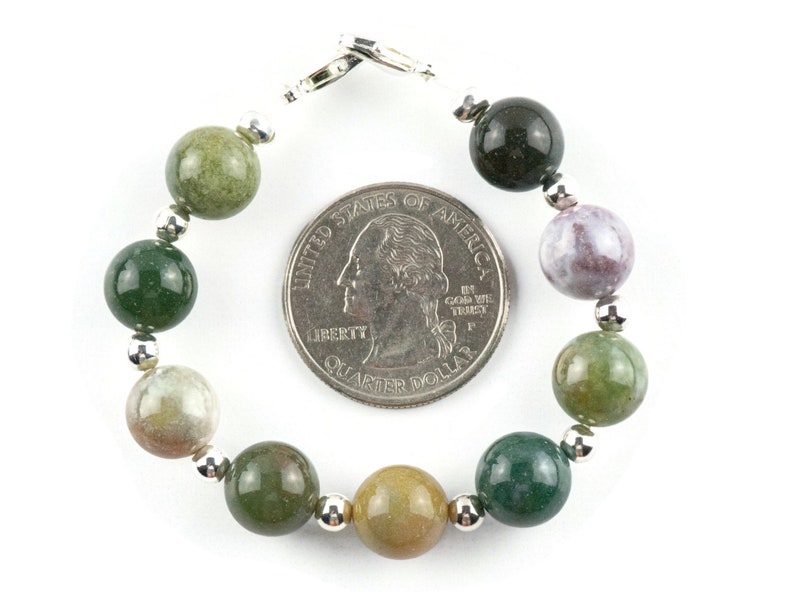 K&ouml;nnte beinhalten: Ein Armband aus gr&uuml;nem, braunem und violettem Achat mit silbernen Perlen und einem silbernen Verschluss. Das Armband ist etwa so gro&szlig; wie eine US-amerikanische 25-Cent-M&uuml;nze.