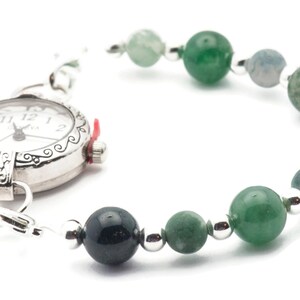 May include: A silver pocket watch with a white face and black hands is attached to a bracelet made of green and grey beads.